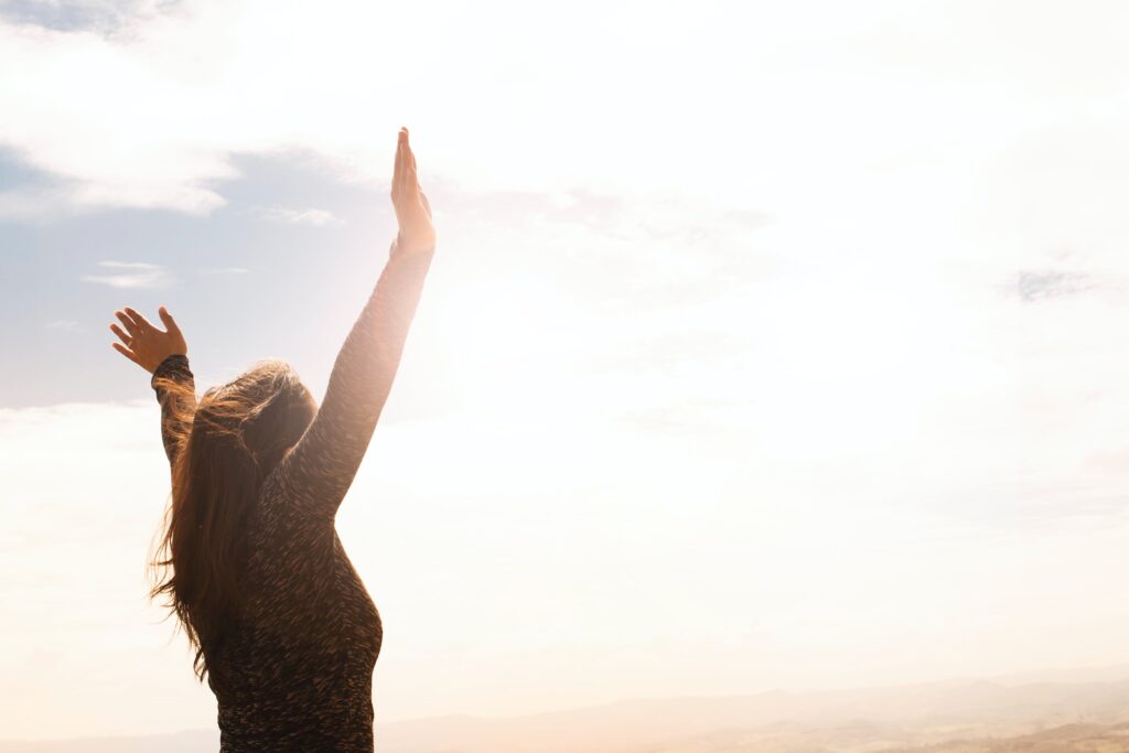 photo of woman standing with her arms in the air showing a sense of freedom. overlooking a misty rolling landscape with light on the horizon