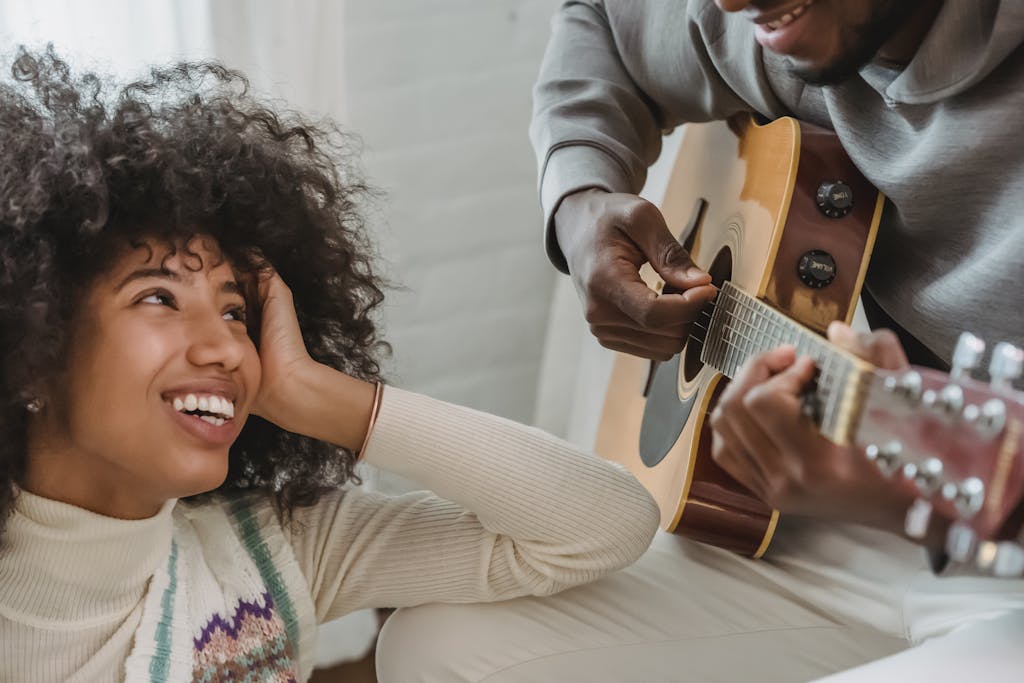 Unrecognizable African American male musician playing acoustic guitar for happy black girlfriend while spending time together in light room at home. Rhythm of Faith and Relief Academy of Inner wisdom blog 